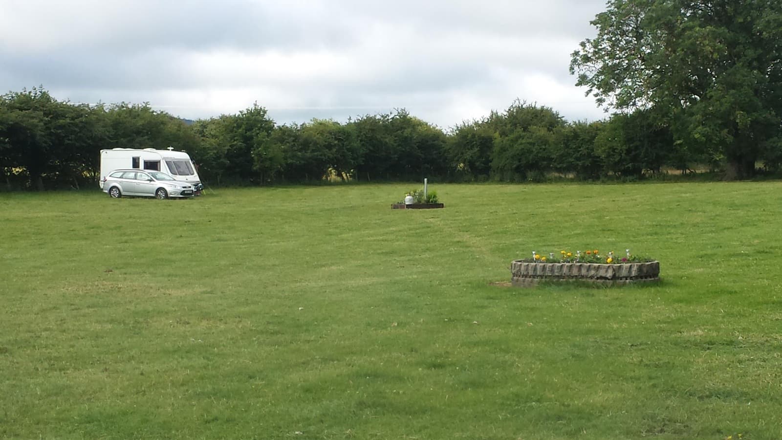 A caravan and car pitched on the open grass, with stone flower planters nearby